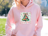 Person wearing a pink hoodie with a colorful Christmas tree design and 'Merry & Bright' text.