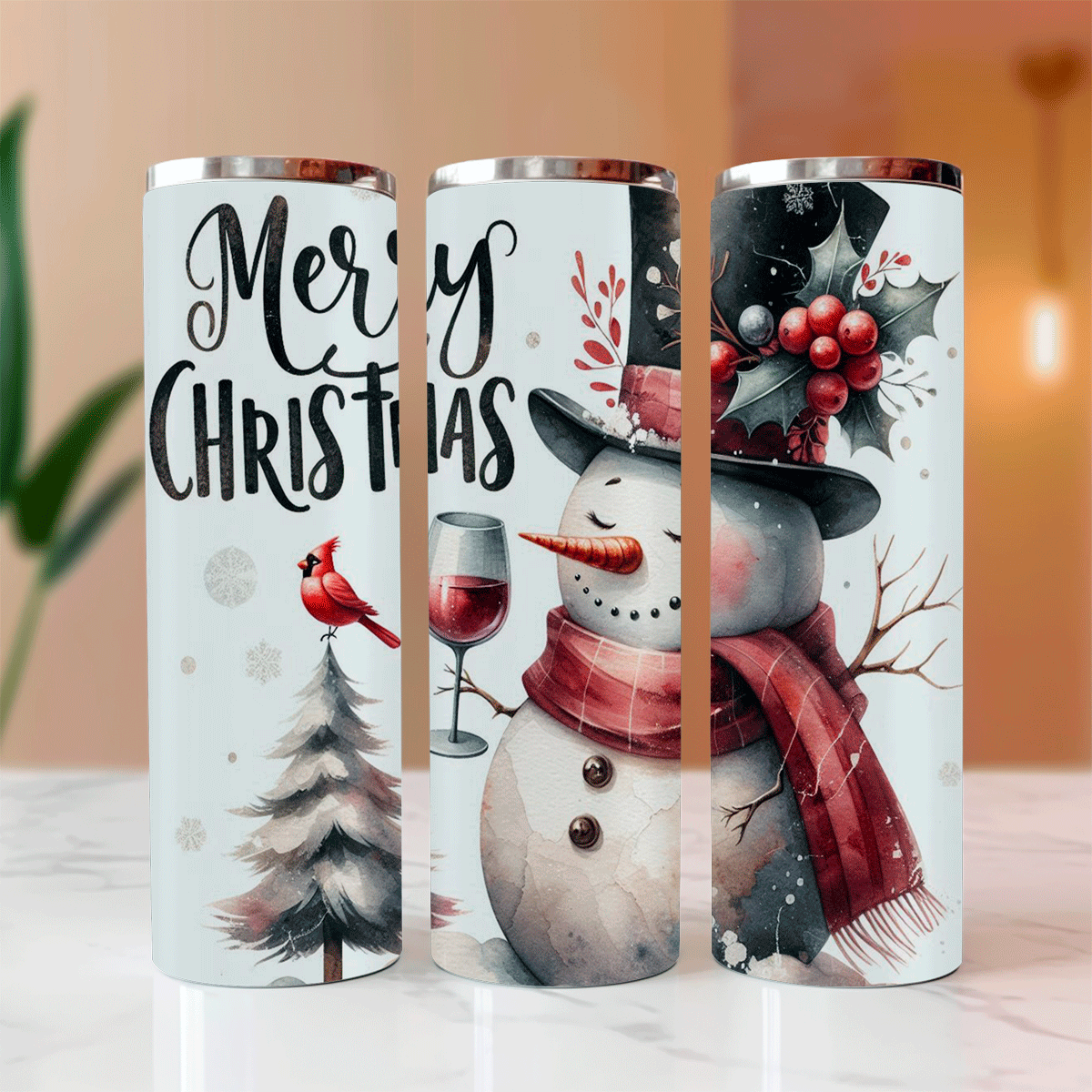 Three Christmas-themed tumblers with snowman, cardinal, and wine glass designs on a blurred indoor background.