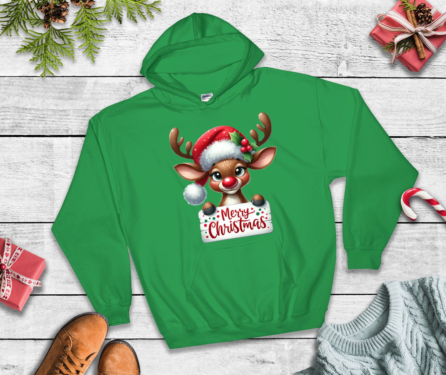 Green hoodie with a reindeer design and 'Merry Christmas' text on a wooden surface with holiday decorations.