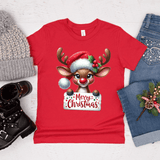 Red t-shirt with a Christmas reindeer design, surrounded by winter accessories on a light wooden surface.