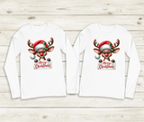 Two white long-sleeve shirts with a Christmas reindeer design on a wooden surface.