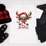 White t-shirt with a reindeer wearing a Santa hat and 'Merry Christmas' text, surrounded by a beanie, slippers, and jeans on a white background.
