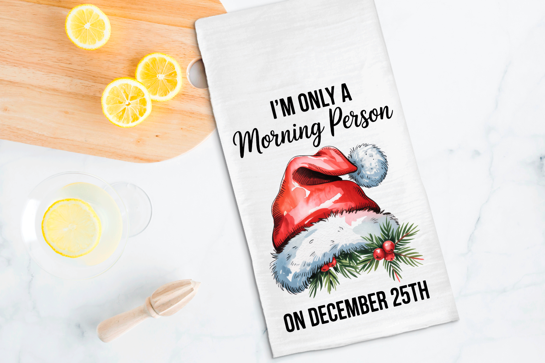 Tea towel with Santa hat and text on a kitchen counter with lemons