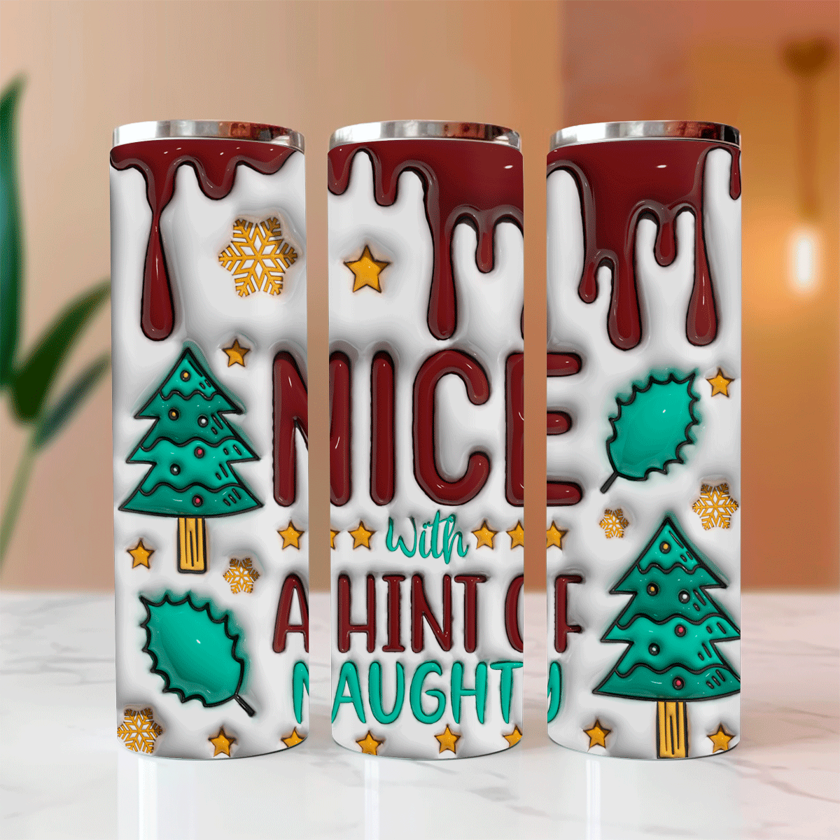 Three stainless steel tumblers with Christmas-themed designs on a marble surface.