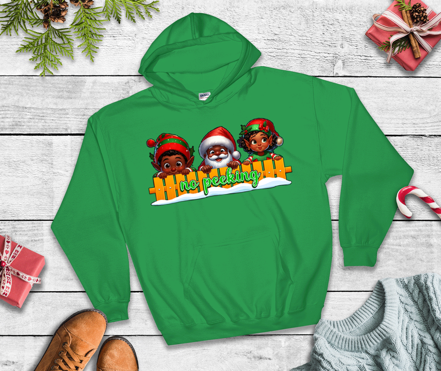 Green hoodie with Christmas-themed design on a wooden surface with festive decorations.