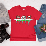 Red t-shirt with Christmas-themed design and text, surrounded by winter accessories on a light wooden surface.
