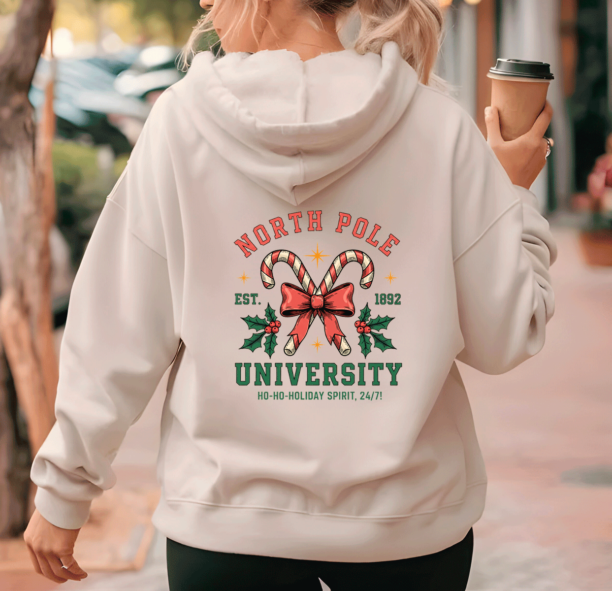 Person wearing a hoodie with 'North Pole University' design, holding a coffee cup.