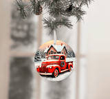 Decorative Christmas ornament with a red truck and cabin design, hanging from a pine branch.