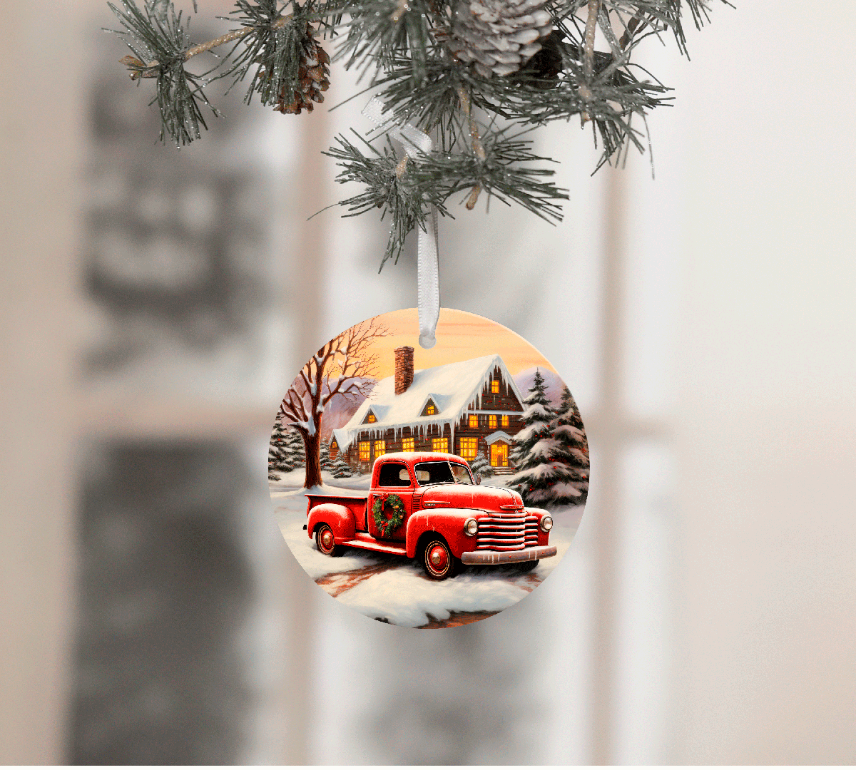 Christmas ornament with a red truck and snowy village scene, hanging from tree branches.