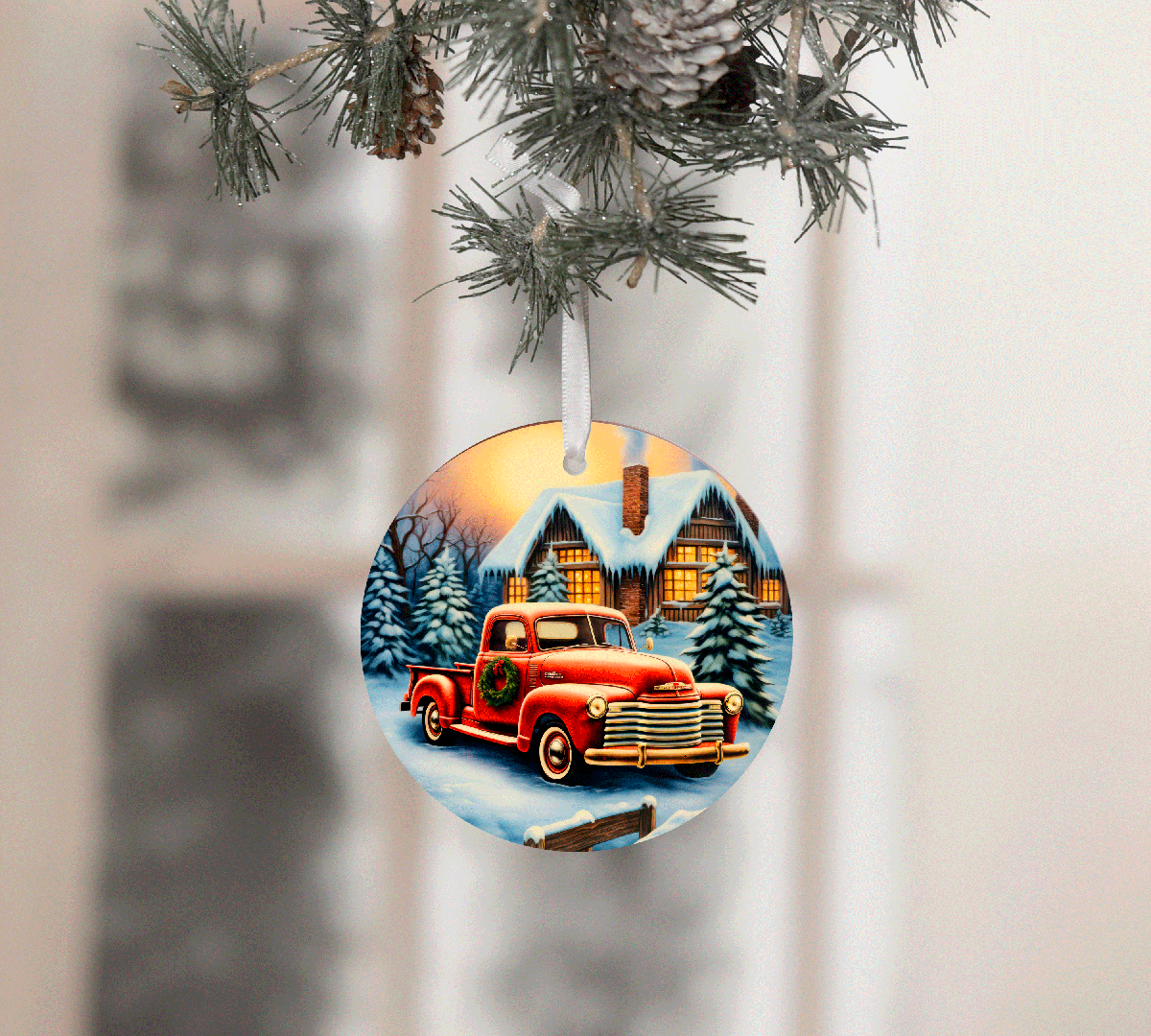 Christmas ornament with a red truck and snowy cabin design, hanging from a tree.