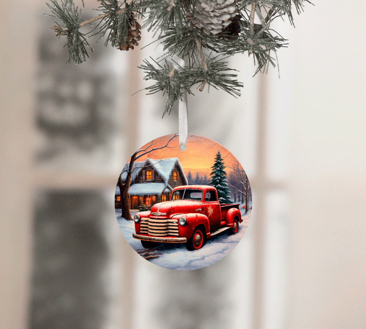 Christmas ornament with a red truck and snowy village scene, hanging from pine branches.