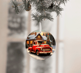 Christmas ornament with a red truck and cabin design, hanging from a tree.