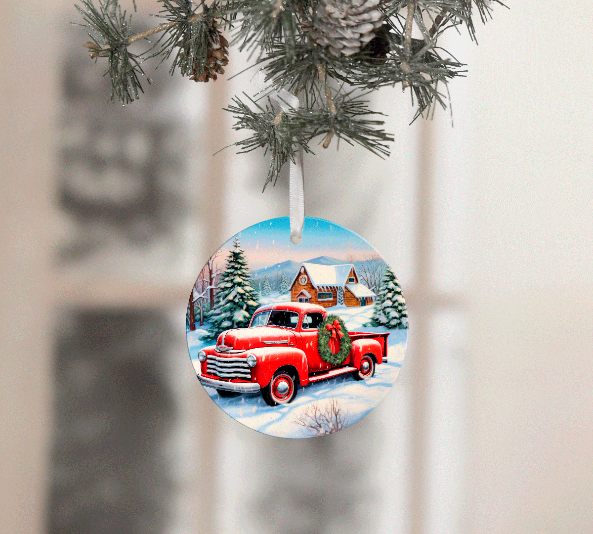 Christmas ornament with a red truck and wreath on a snowy scene, hanging from a tree.