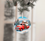 Christmas ornament with a red truck and wreath on a snowy scene, hanging from a tree.