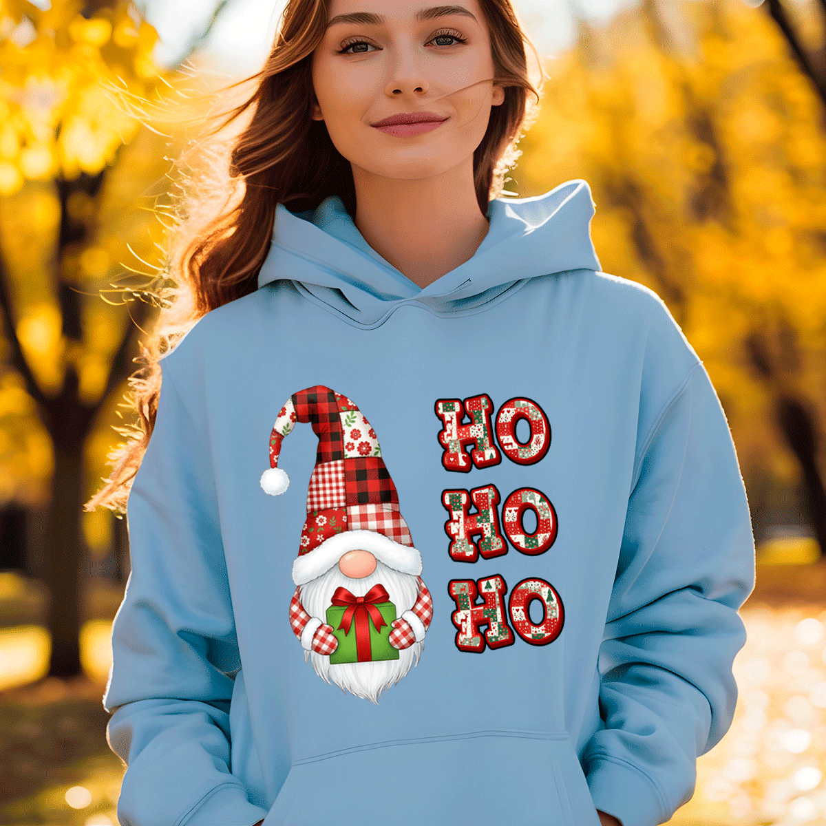 Person wearing a light blue hoodie with a Christmas-themed design featuring a gnome and 'HO HO HO' text, standing in an autumn setting.
