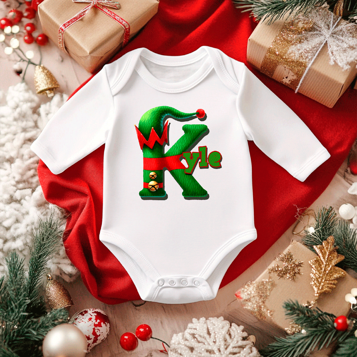 White baby onesie with a green and red design on a red fabric background with Christmas decorations.