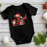 Black baby onesie with Christmas-themed design on a wooden surface.