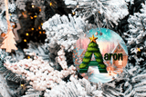 Decorative Christmas ornament with a tree design and 'aron' text, hanging on a frosted Christmas tree.