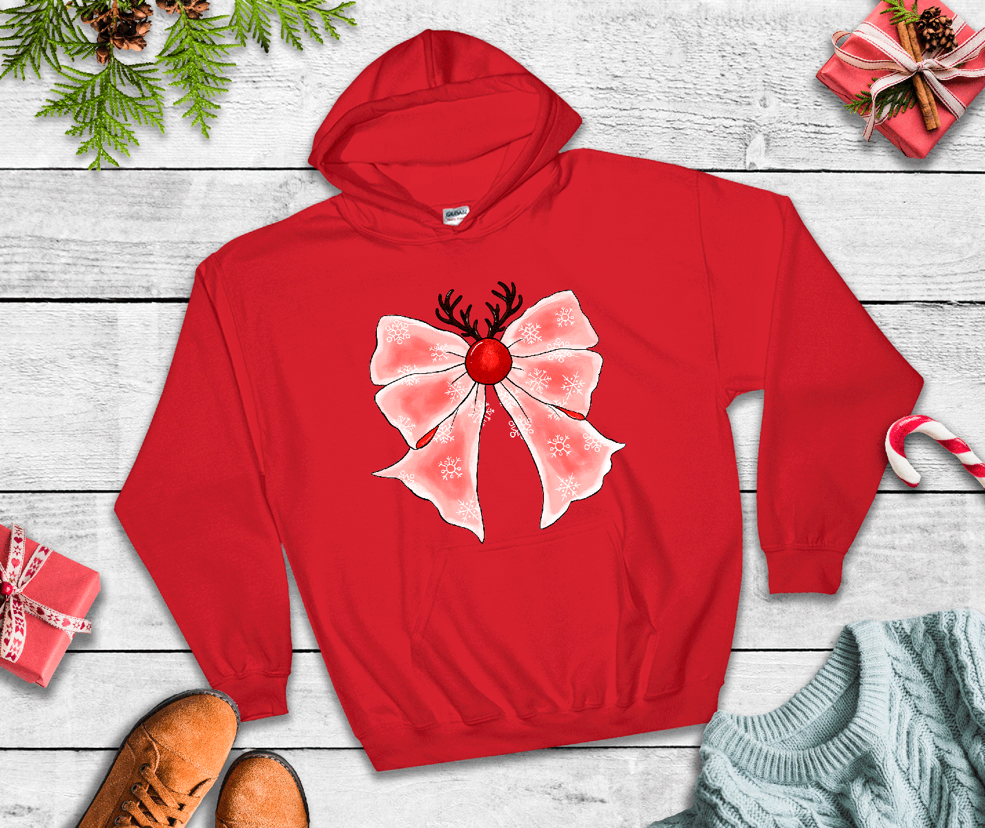Red hoodie with a pink bow and reindeer design on a wooden surface with Christmas decorations.