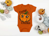 Orange baby onesie with pumpkin design and text on a white background with decorative pumpkins and skulls.