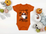 Orange baby onesie with Halloween design featuring an owl and text, surrounded by pumpkins and decorative items on a white background.