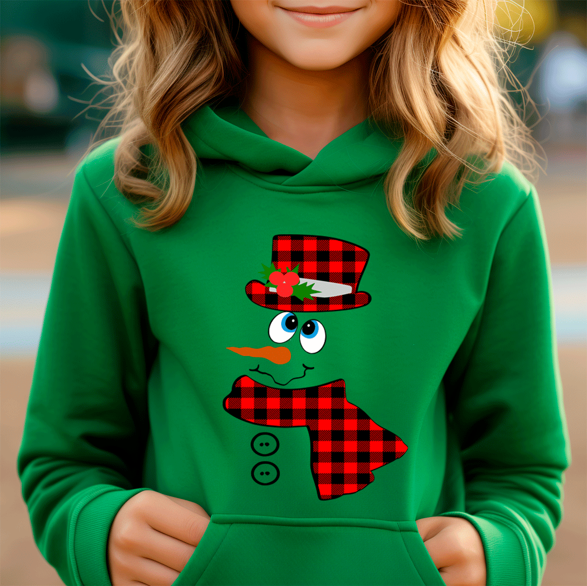 Child wearing a green hoodie with a snowman design featuring a red plaid hat and scarf.