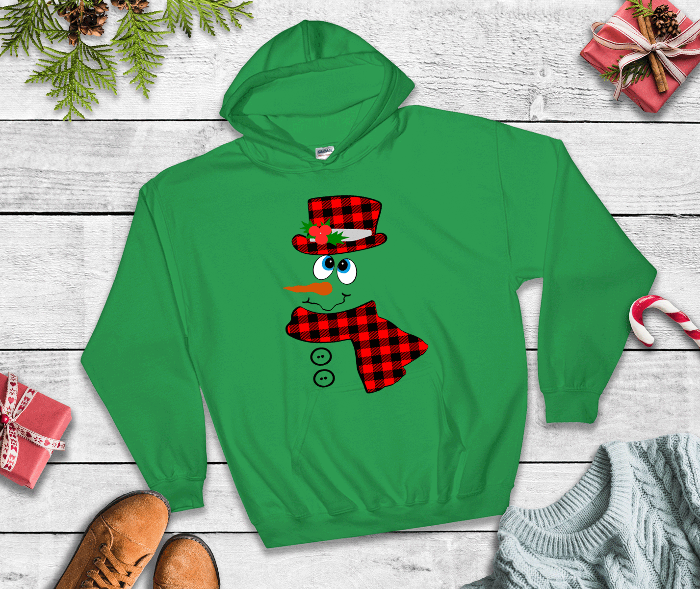 Green hoodie with a snowman design on a wooden surface with Christmas decorations.