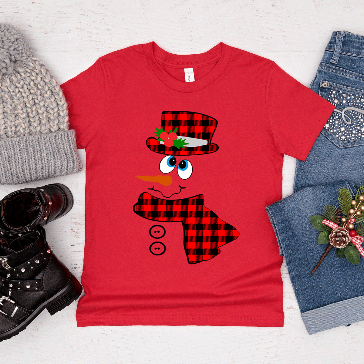 Red t-shirt with a snowman design surrounded by winter accessories on a light background