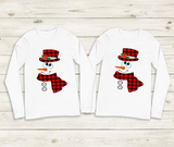 Two white long-sleeve shirts with snowman designs on a wooden surface