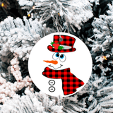 Snowman ornament with plaid hat and scarf hanging on a Christmas tree.