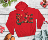 Red hoodie with 'Reindeer Games' text on a wooden surface with Christmas decorations.