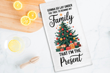 Tea towel with Christmas tree design and humorous text on a kitchen counter with lemons and a wooden spoon.