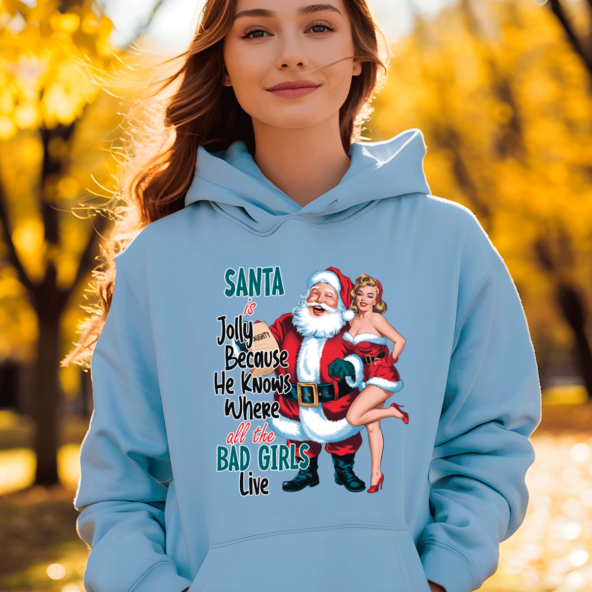 Person wearing a light blue hoodie with a graphic design featuring Santa Claus and text, standing in an outdoor setting with trees.