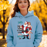 Person wearing a light blue hoodie with a graphic design featuring Santa Claus and text, standing in an outdoor setting with trees.