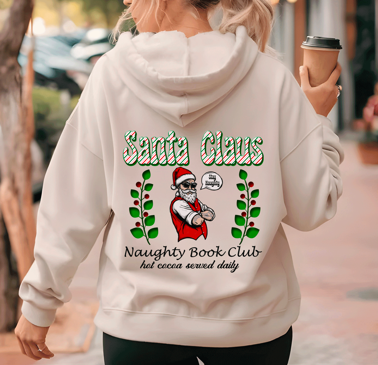 Person wearing a hoodie with 'Santa Claus Naughty Book Club' design, holding a coffee cup.