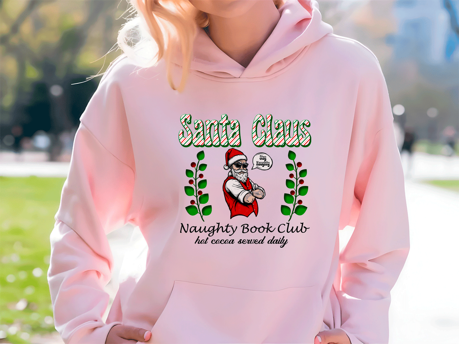 Person wearing a pink hoodie with 'Santa Claus Naughty Book Club' design outdoors.