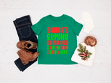 Green t-shirt with Christmas-themed text, paired with jeans, boots, and a decorative item on a light background