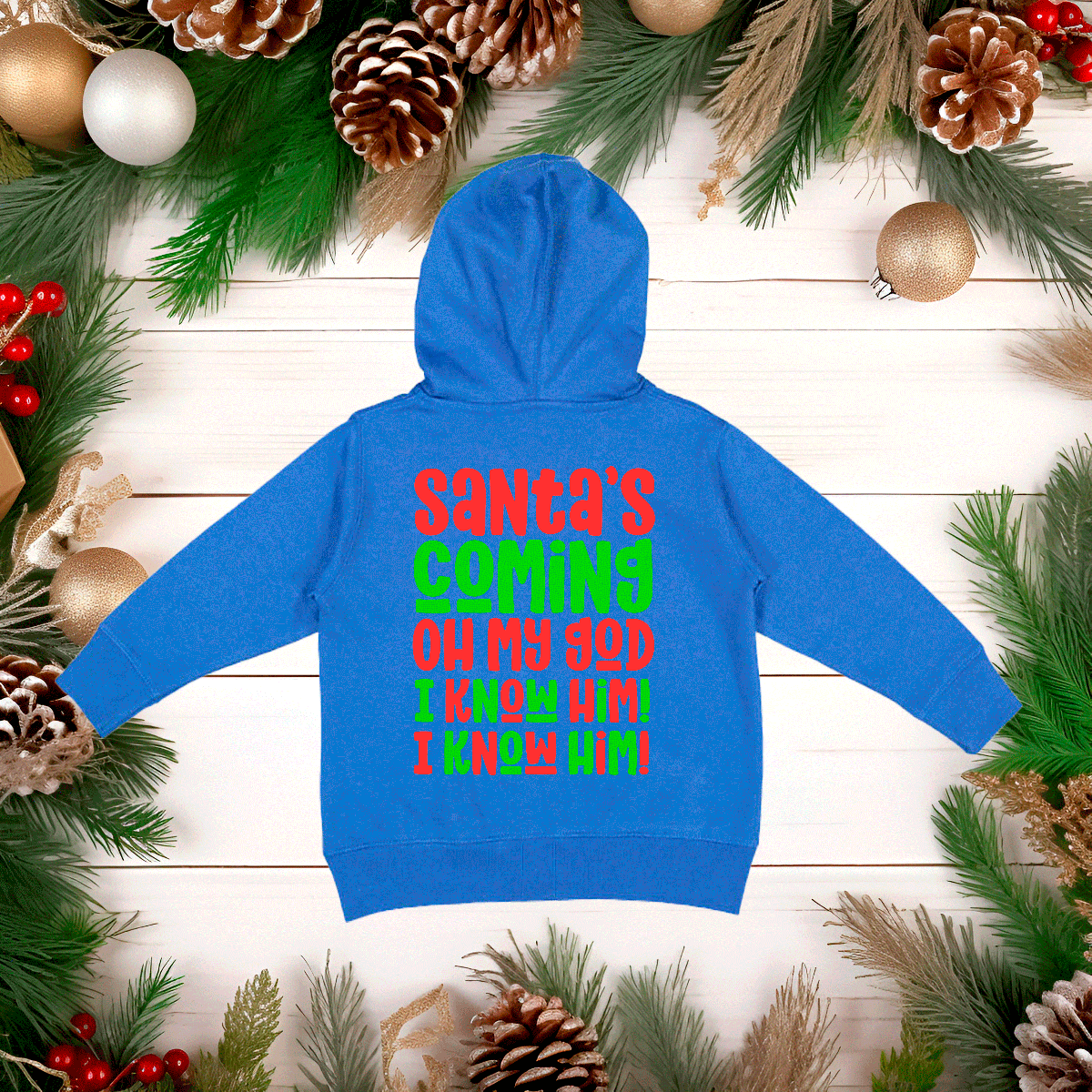 Blue hoodie with colorful text on a wooden surface surrounded by Christmas decorations
