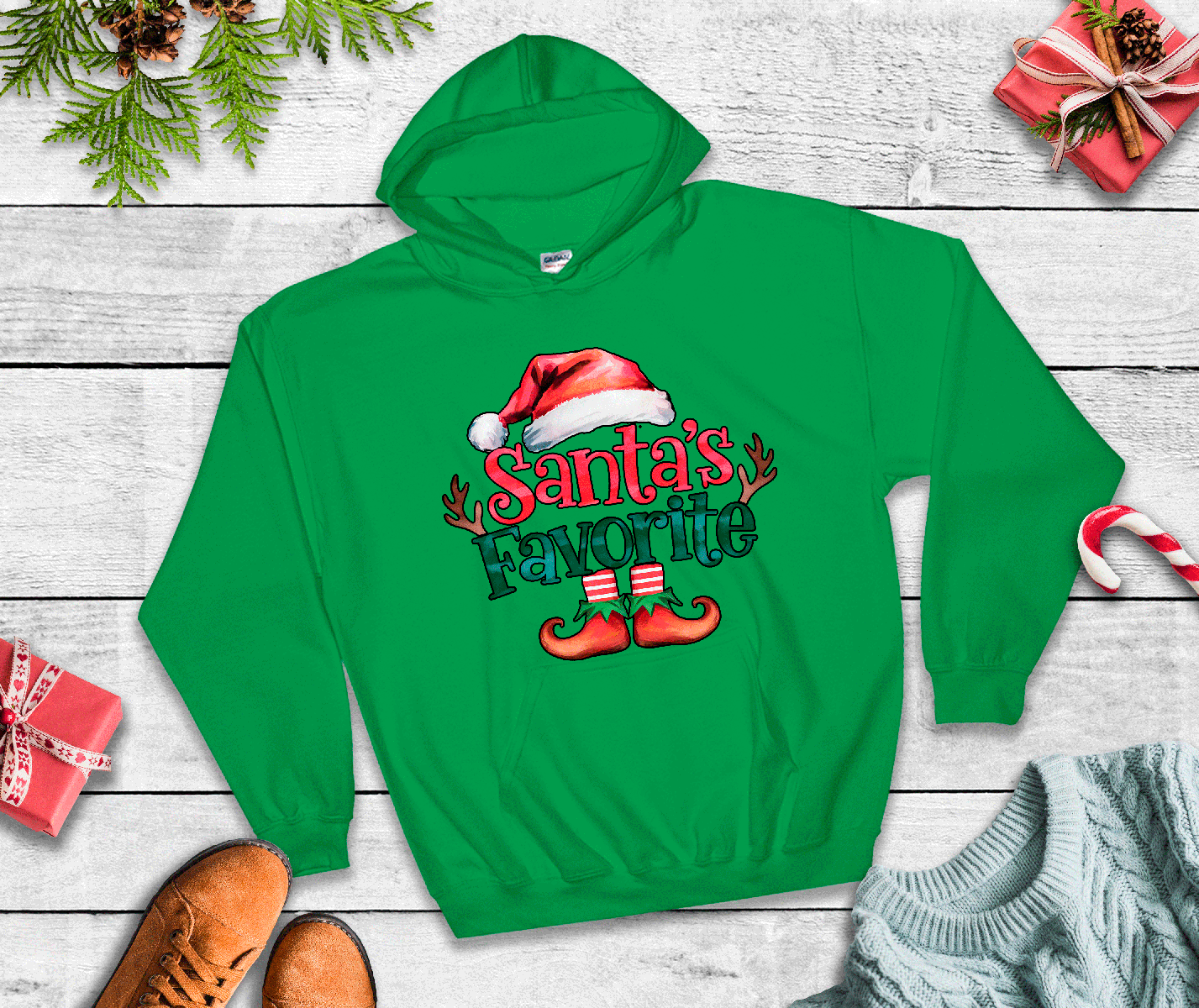 Green hoodie with 'Santa's Favorite' text on a wooden surface with Christmas decorations.