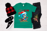 Green t-shirt with a skeleton design and text, surrounded by a beanie, shoes, jeans, and a small tree decoration on a light background.