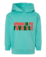 Turquoise hoodie with 'Smiling is my favorite' text in red and green on a white background