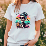 Person wearing a white t-shirt with a 'Spooky Mama' skeleton design in a field.
