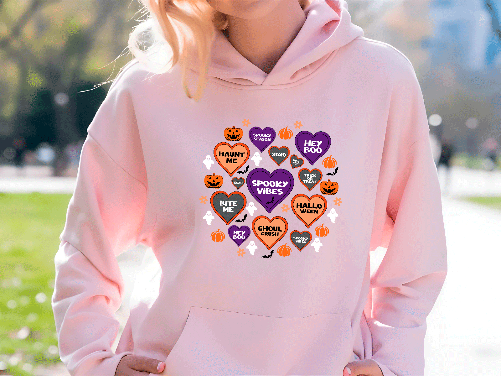 Person wearing a pink hoodie with Halloween-themed designs outdoors.