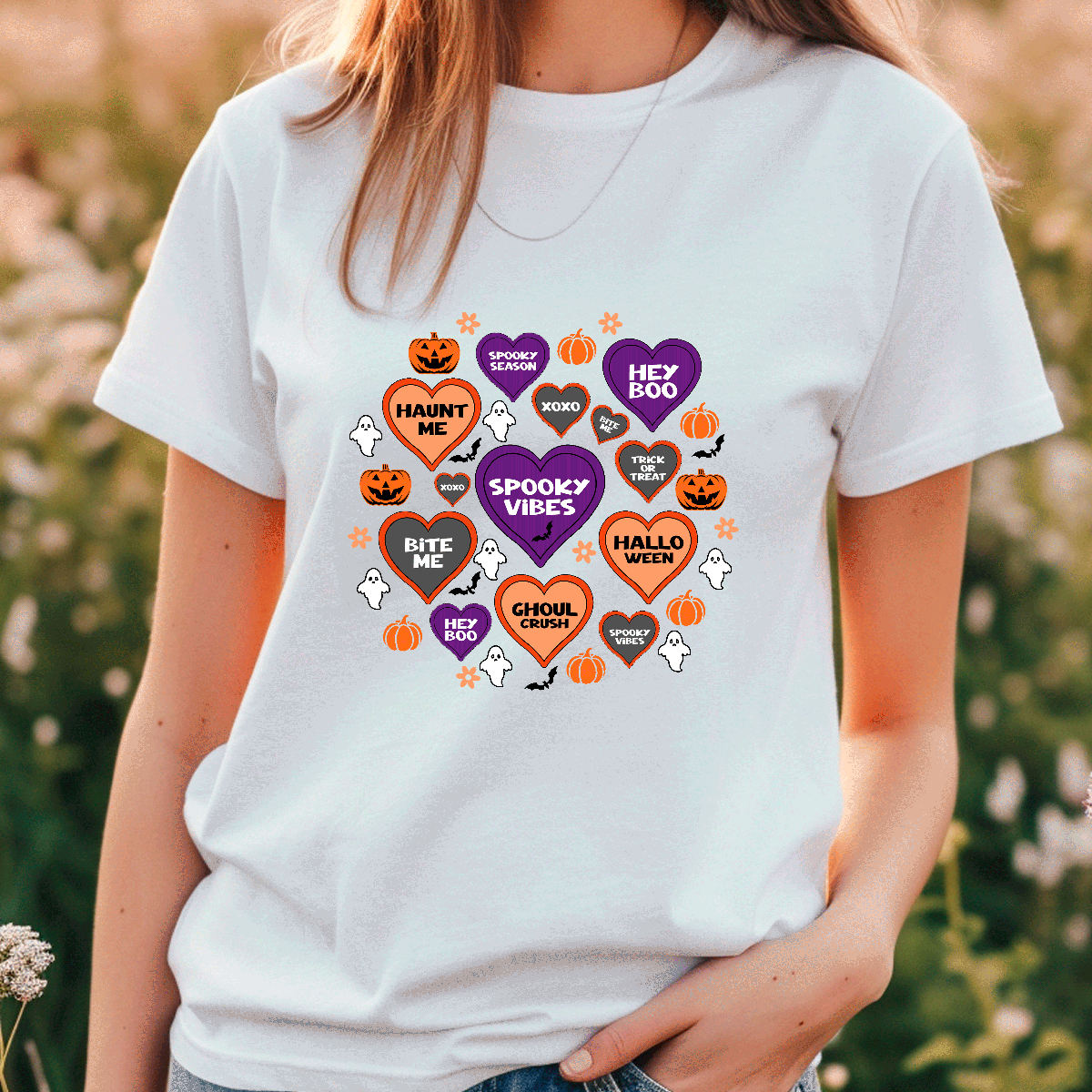 Person wearing a white t-shirt with Halloween-themed graphics in a field.