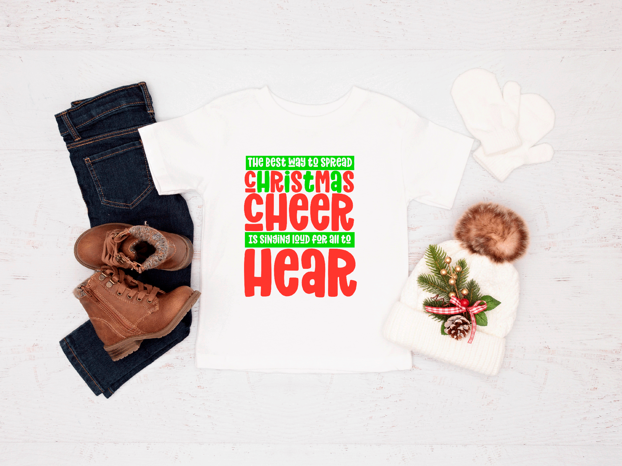 Holiday-themed shirt with text and festive design, paired with jeans and boots on a white background.