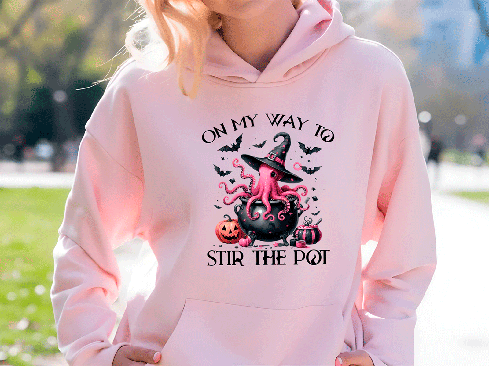 Person wearing a pink hoodie with Halloween-themed design outdoors.