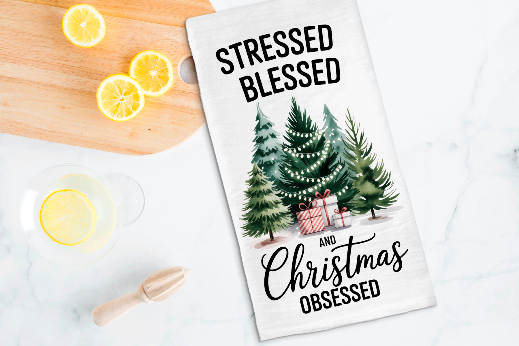Tea towel with Christmas design and text on a kitchen counter with lemons and a wooden spoon.