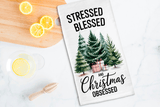 Tea towel with Christmas design and text on a kitchen counter with lemons and a wooden spoon.
