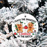 Christmas ornament with gingerbread men and text 'I teach the smartest cookies in the batch' on a snowy tree background.