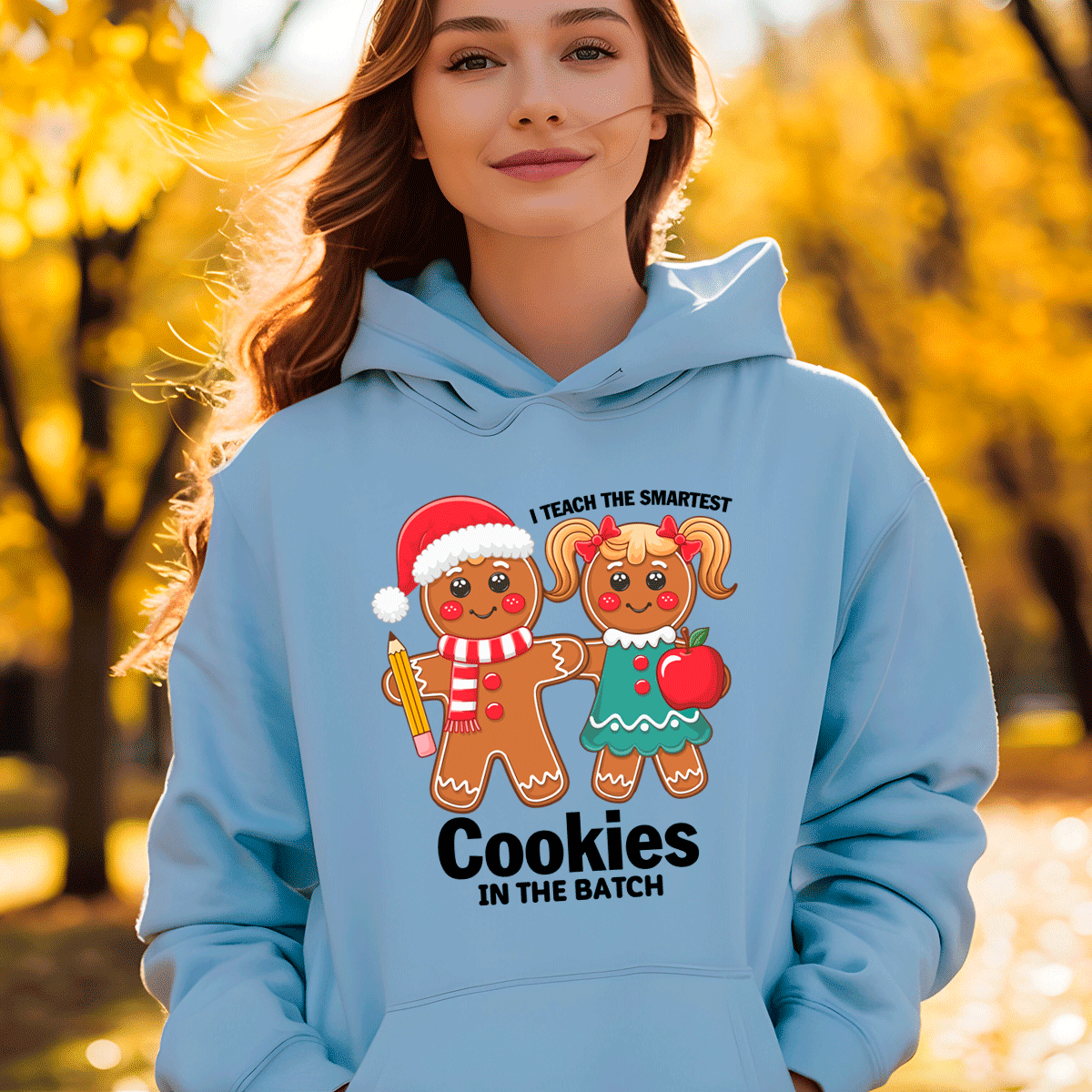 Person wearing a light blue hoodie with a gingerbread design and text, standing outdoors with trees in the background.